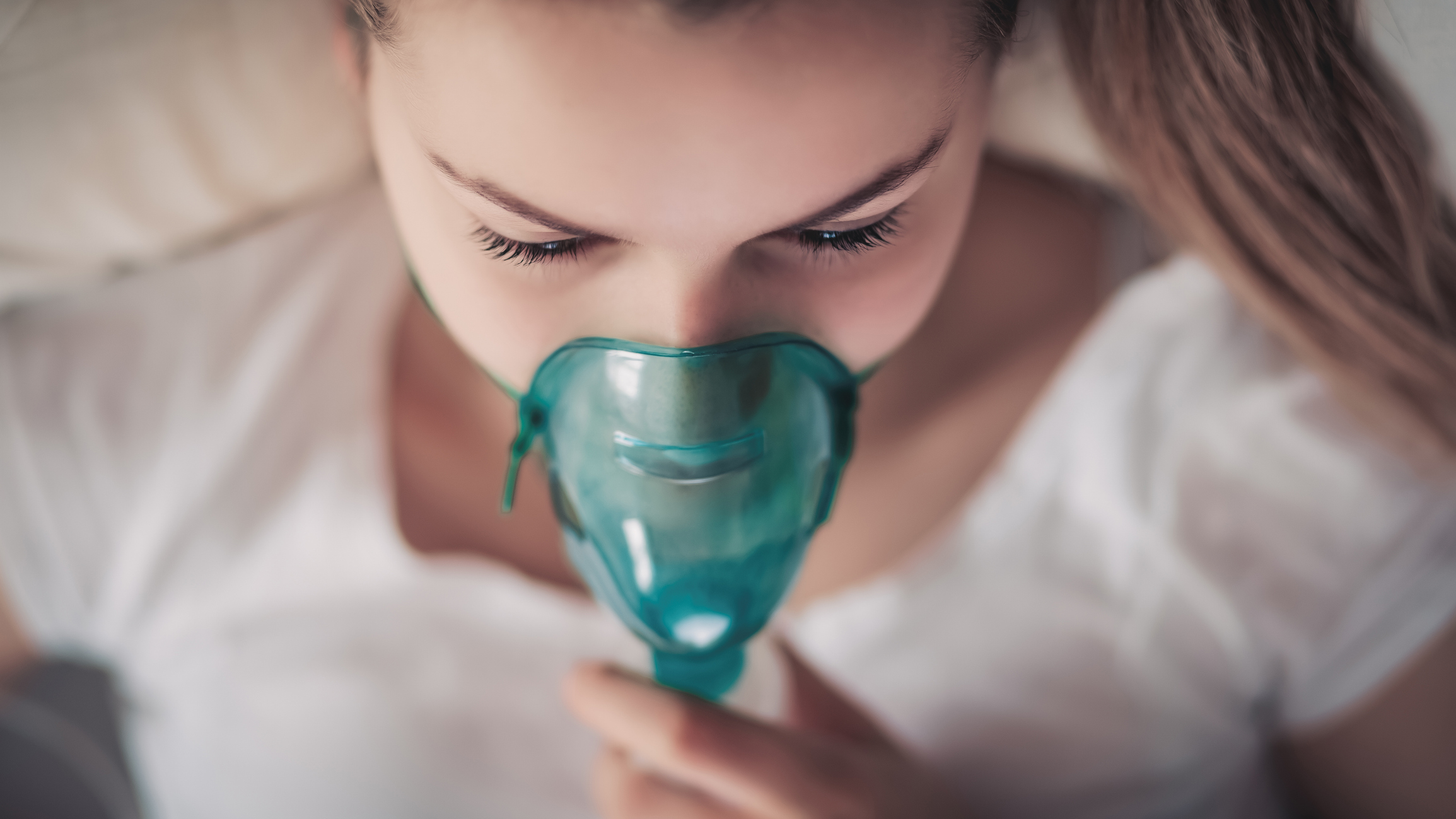 Top View of a Young Woman Using a Teal Oxygen Mask for Respiratory Care — Hutchinson, MN — Corner Home Medical
